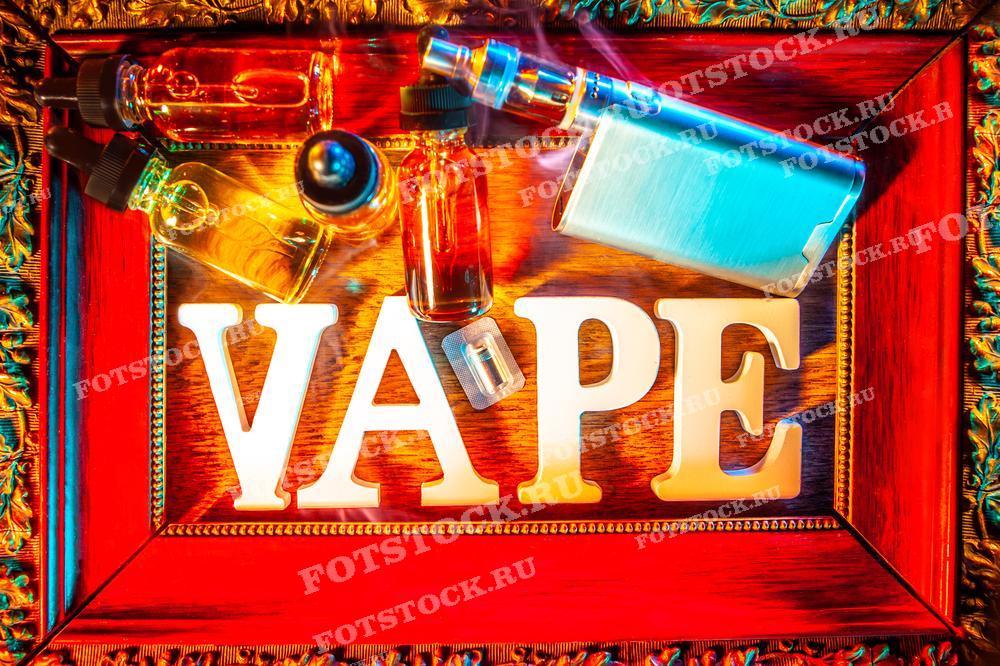 На фотографии изображены буквы, составляющие слово "VAPE", и различные аксессуары для вейпинга, такие как флаконы с жидкостью и электронные устройства, расположенные внутри декоративной рамки.